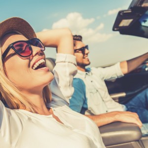 Freedom of the open road. Side view of joyful young woman relaxing on the front seat while her boyfriend sitting near and driving their convertible