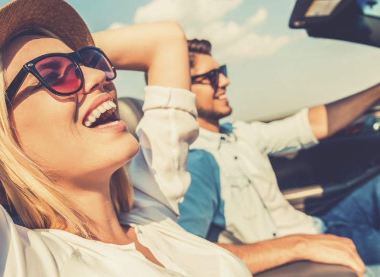 Freedom of the open road. Side view of joyful young woman relaxing on the front seat while her boyfriend sitting near and driving their convertible